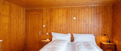 Una habitación con paneles de madera, una cama, mesitas de noche y una puerta.