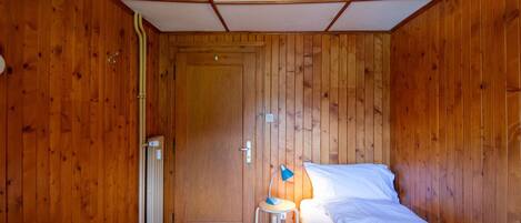 A small, cozy room with wooden walls and a single bed.