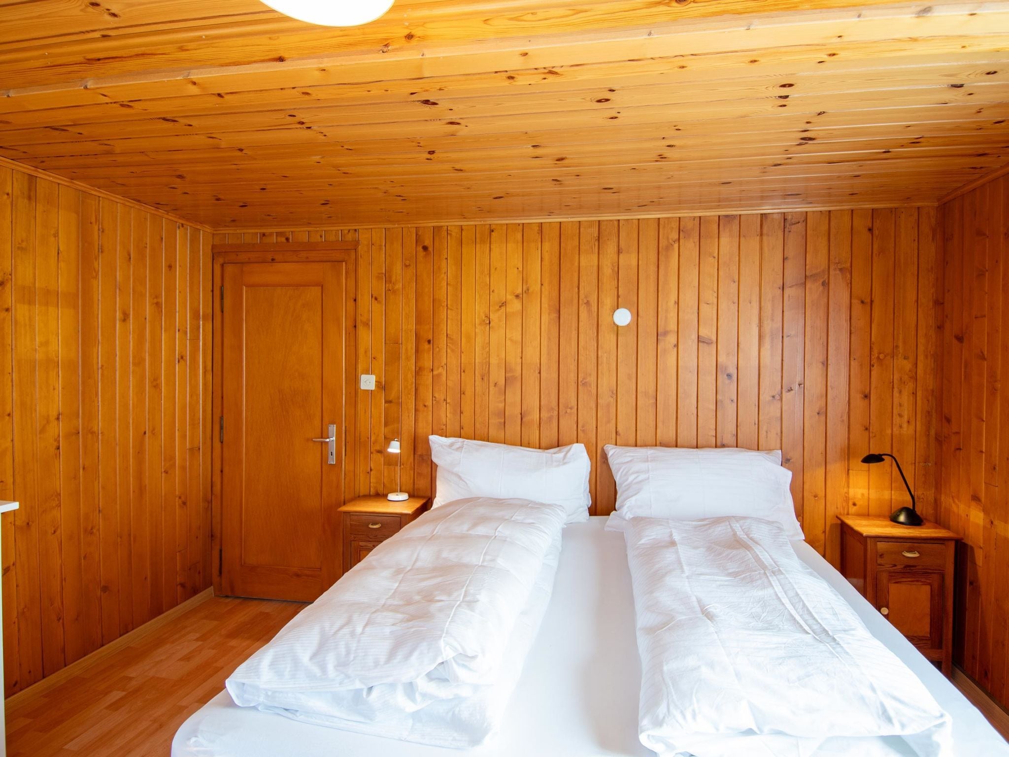 A wooden-paneled room with a bed, two bedside tables, and a door.