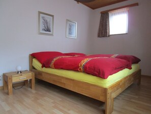 Ein Einzelbett mit Holzbettrahmen, ein Nachttisch mit Lampe und zwei gerahmte Bilder an der Wand.