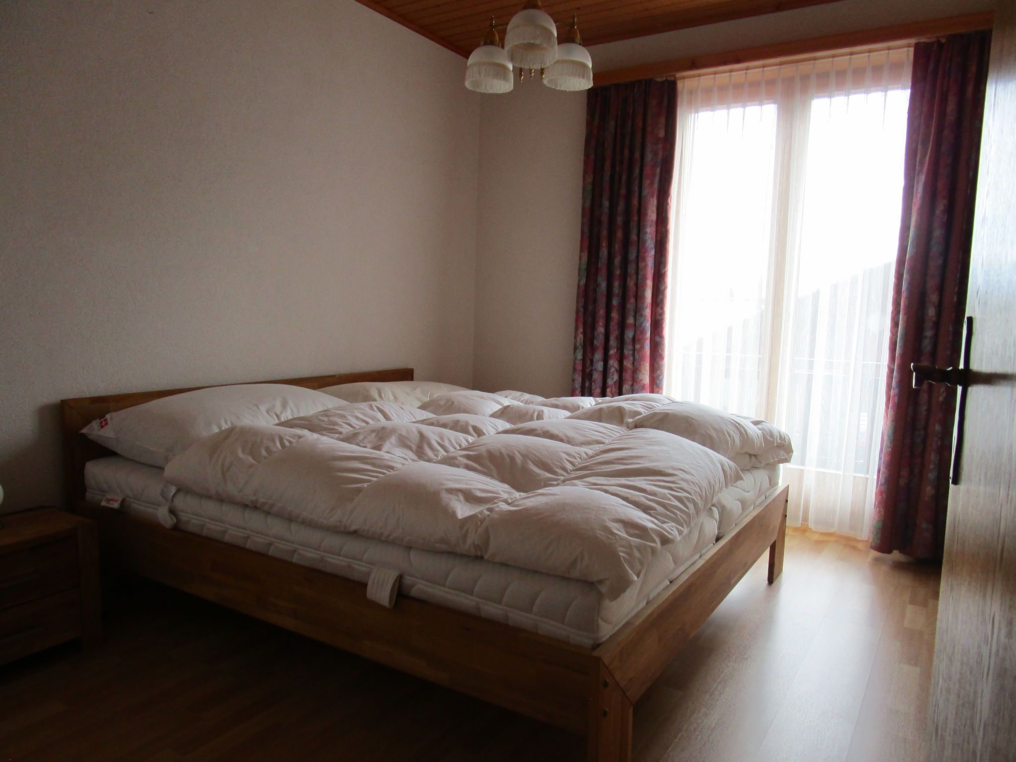 Un dormitorio con cama de madera, mesita de noche, candelabro y ventana con cortinas.