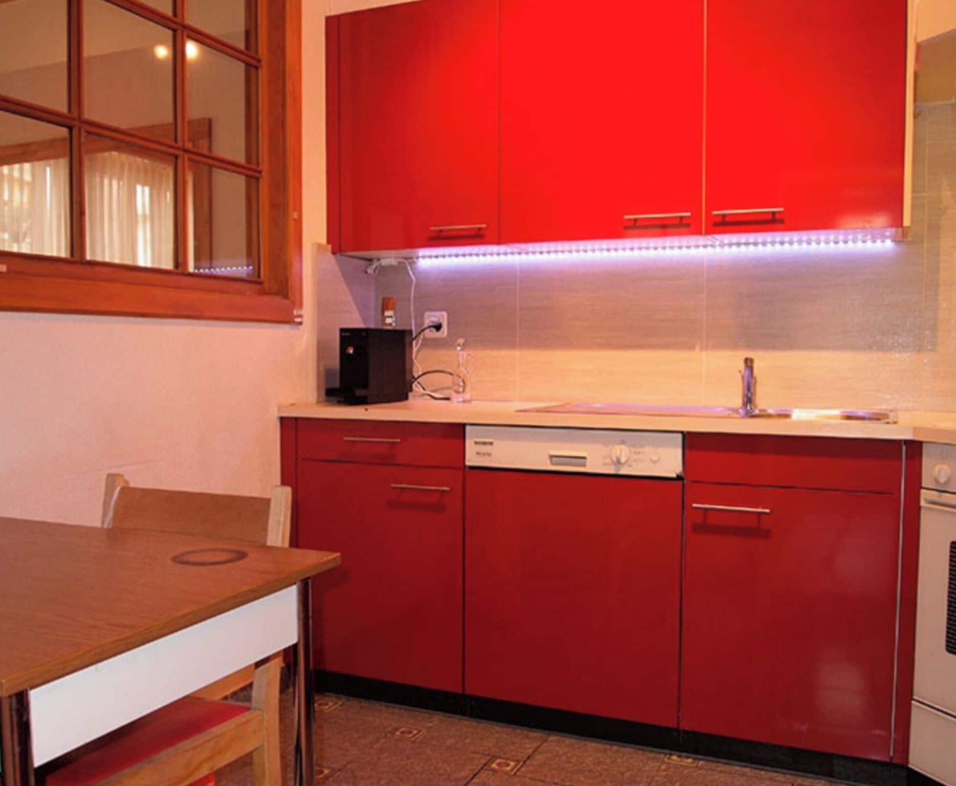 A kitchen with red cabinets, a dishwasher, and a window with curtains.