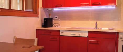 A kitchen with red cabinets, a dishwasher, and a window with curtains.