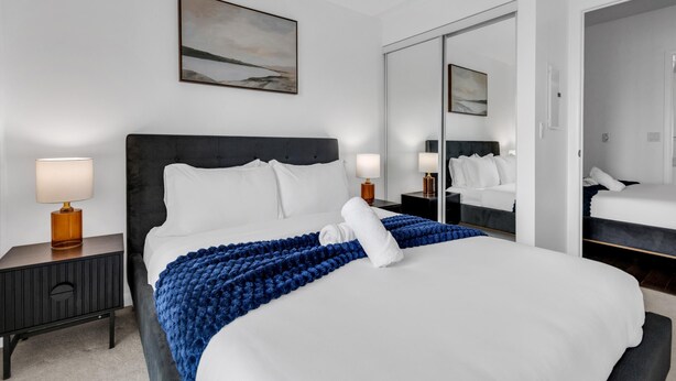 Ett hotellrum med en stor säng, två sängbord med lampor, en spegel och en tavla på väggen.