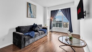 Ett modernt vardagsrum med en grå soffa, ett soffbord i glas och ett stort fönster med gardiner.