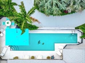Une piscine sur le toit, avec une eau d’un bleu cristallin, entourée de chaises longues blanches et d’une petite table.