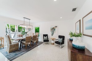 A modern dining area with a white table, wicker chairs, and a hanging light fixture. - New Boutique Juno Retreat | Pool I Steps to Beach! (Juno Beach)