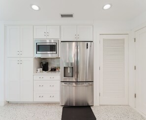 A modern kitchen with white cabinetry, a stainless steel refrigerator, a built-in microwave, and a coffee maker. - New Boutique Juno Retreat | Pool I Steps to Beach! (Juno Beach)