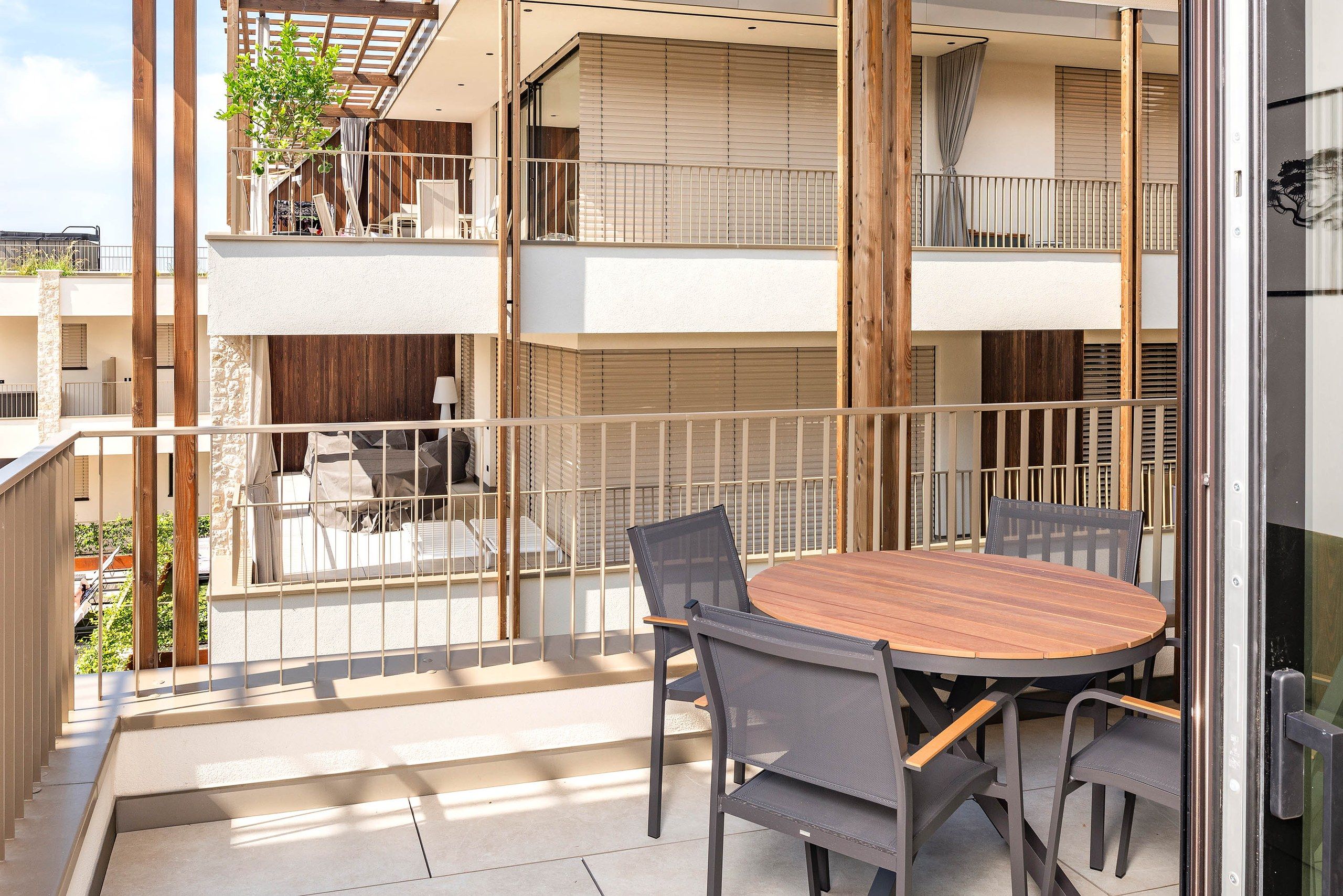Un balcon avec une table et des chaises, une clôture en bois et une vue sur l’intérieur du bâtiment.