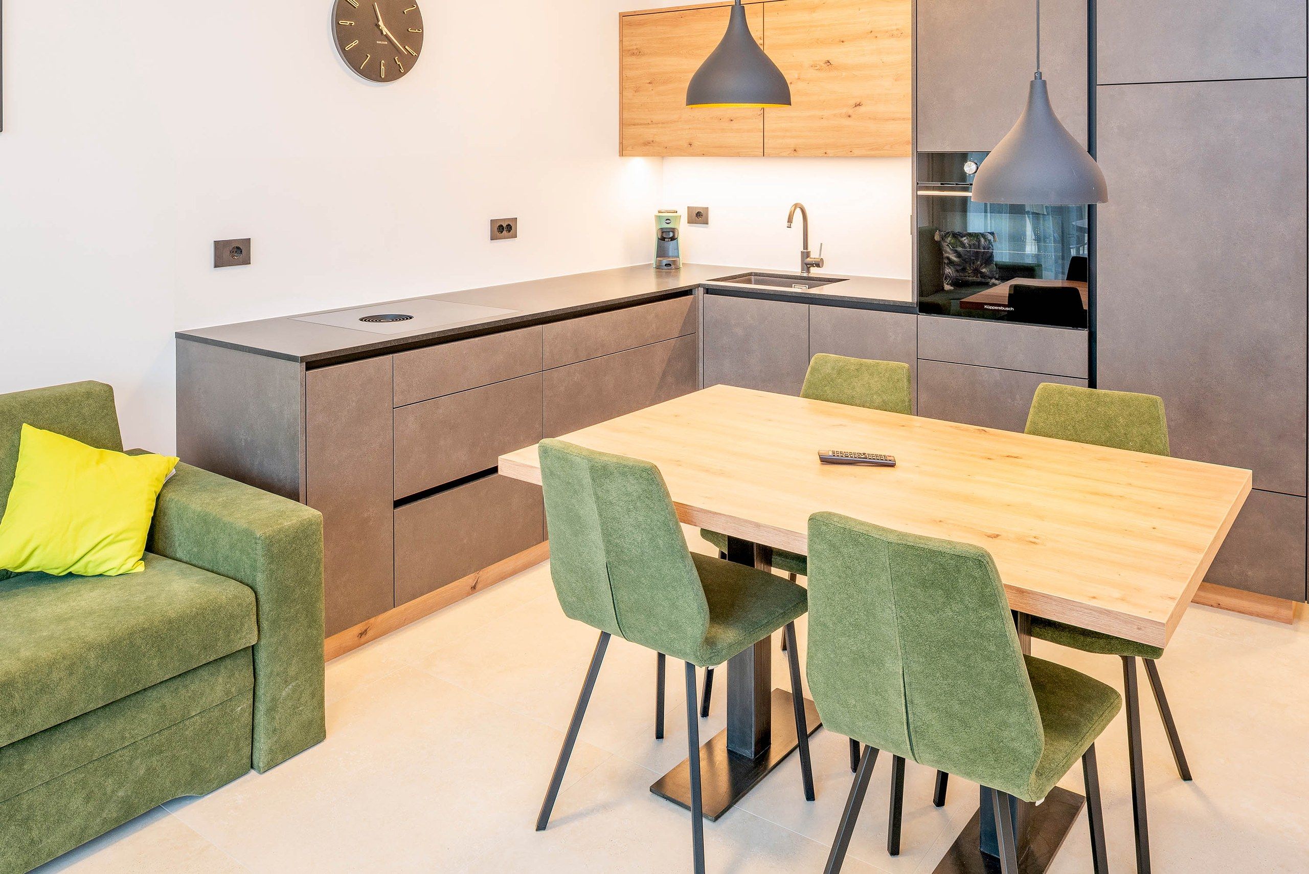 Une cuisine moderne avec un coin repas, comprenant une table en bois et des chaises recouvertes d’un tissu vert.