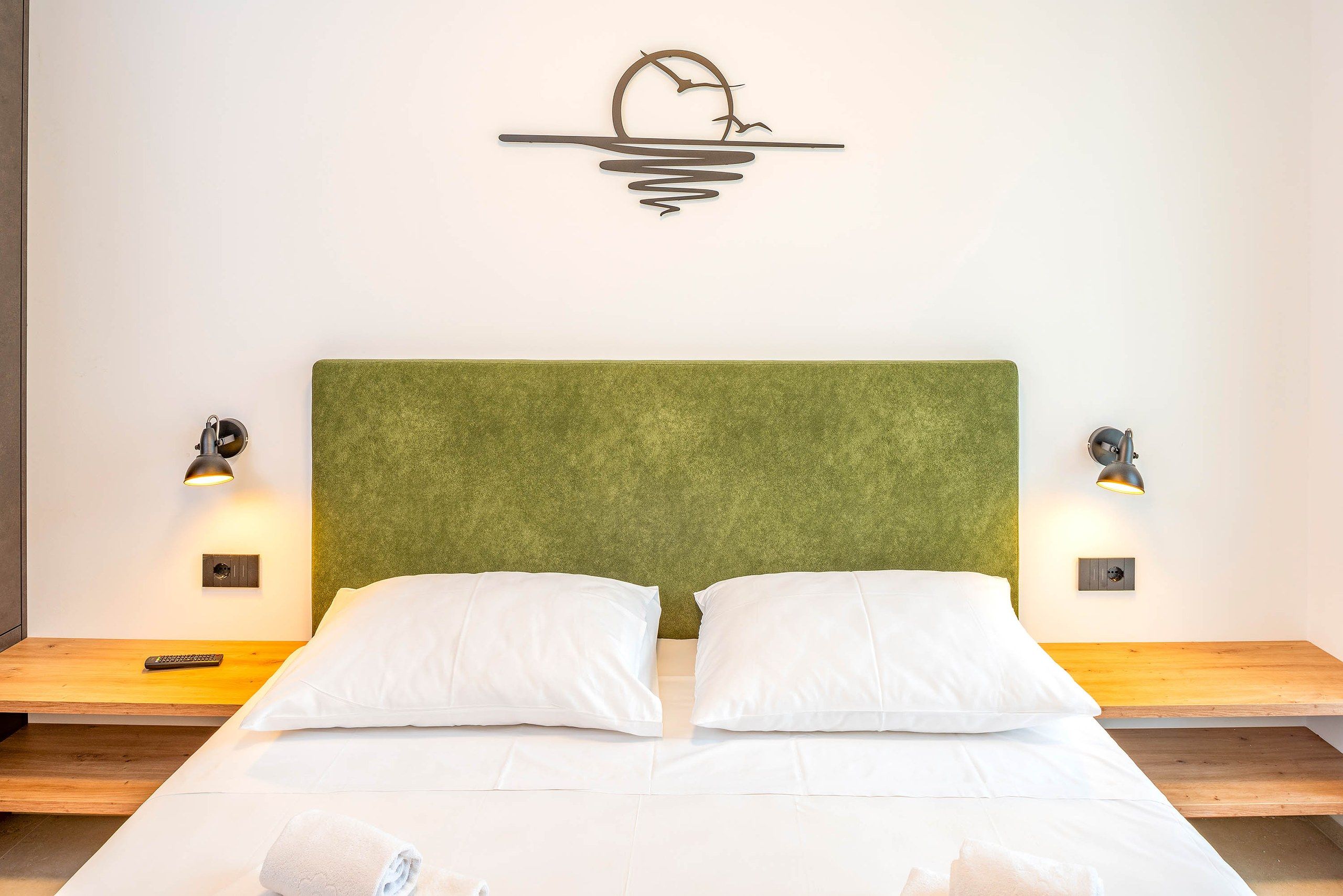 Una cama con cabecera verde, dos almohadas blancas y dos lámparas de pared a cada lado.