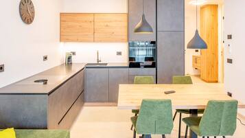 A modern kitchen with a central island, a dining area with a wooden table and green upholstered chairs, and a clock on the wall.