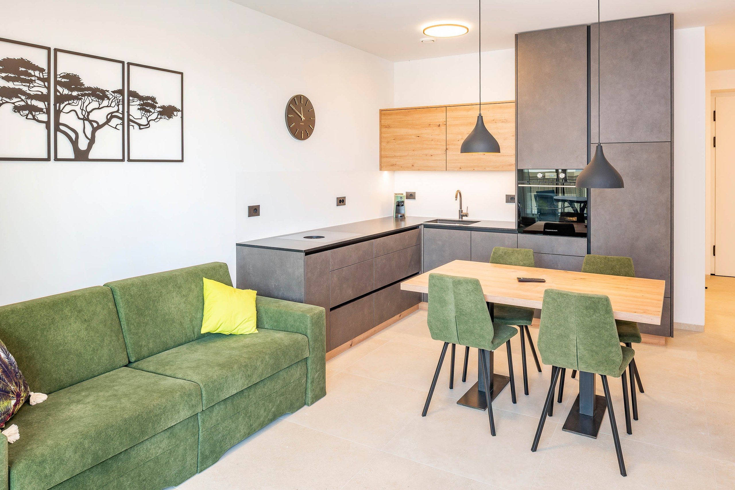 A modern kitchen with a dining area, green upholstered sofa, and artwork on the wall.