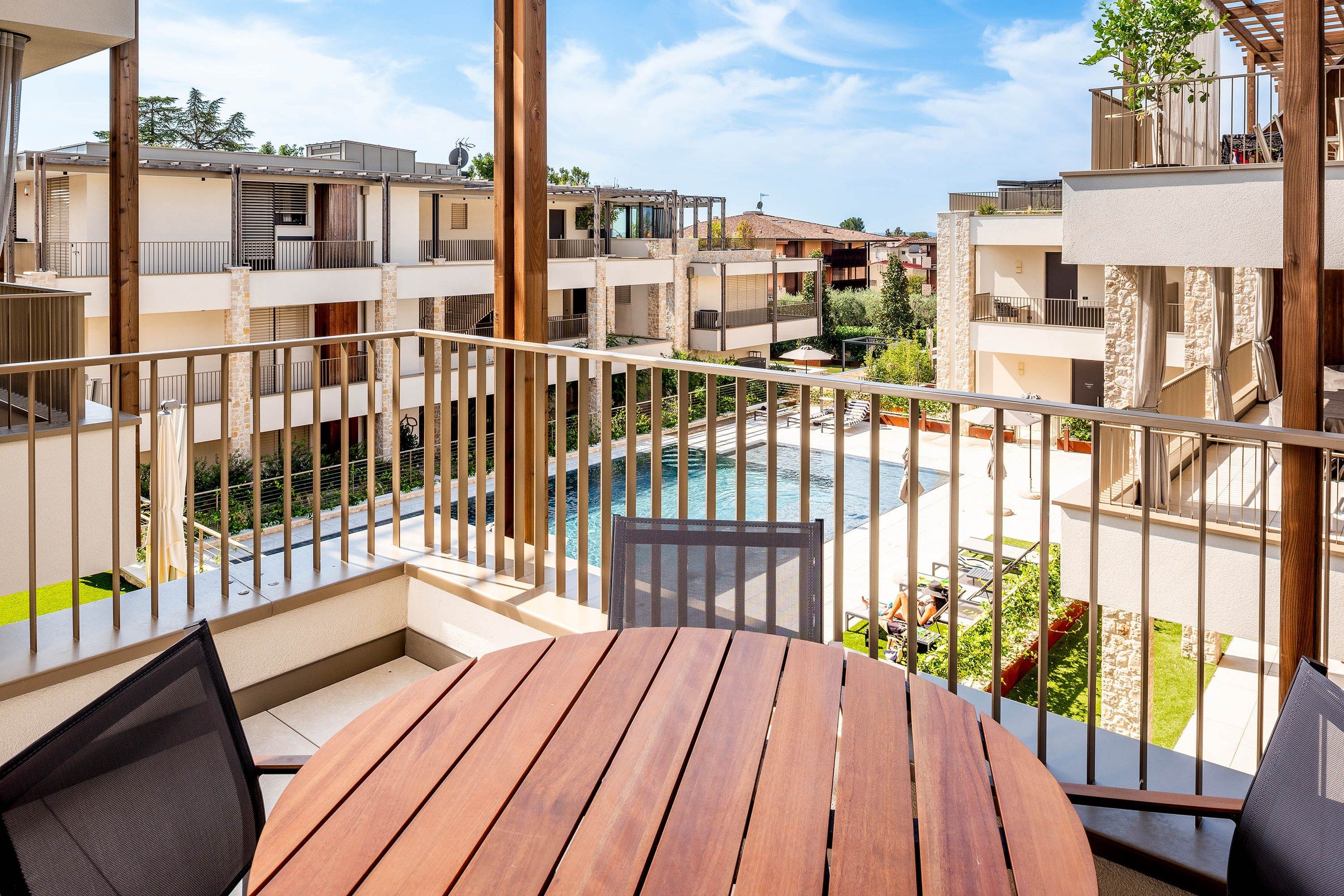 Un balcon avec une table et des chaises en bois, donnant sur une piscine et un jardin.