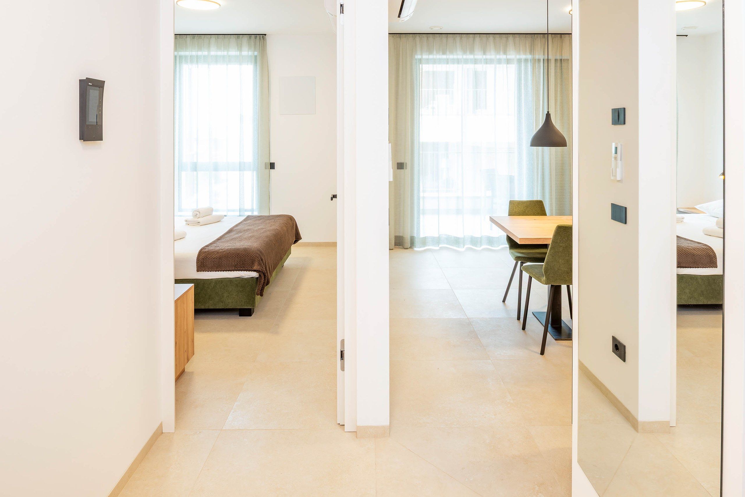 Une chambre d’hôtel avec un lit, un bureau et une chaise. Il y a une fenêtre avec des rideaux et une porte.