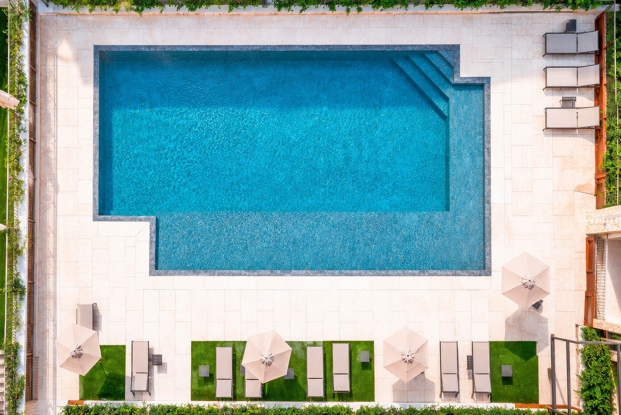 Une piscine rectangulaire à l’eau d’un bleu limpide, entourée d’une terrasse carrelée agrémentée de chaises longues et de parasols.