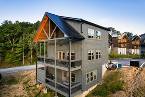 A multi-story building with a balcony on the second floor, a sloped roof, and a view of the surrounding forest. - Smokiedoki Lodge - 3 Ensuite Bedrooms + Loft Near Parkway (Pigeon Forge)