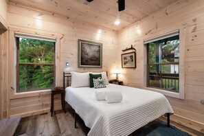 A wooden cabin bedroom with a large bed, two windows, a framed picture, and a nightstand. - Smokiedoki Lodge - 3 Ensuite Bedrooms + Loft Near Parkway (Pigeon Forge)