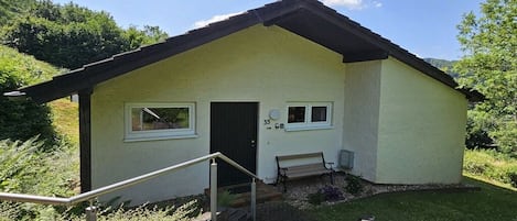 Un edificio pequeño con una puerta, ventanas, un banco y una escalera que lleva a la entrada.