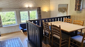 A dining area with a table and chairs, a bench, and a view of greenery outside.