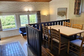 A dining area with a table and chairs, a bench, and a view of greenery outside.