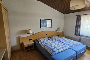 A bedroom with a wooden headboard, two bedside tables with lamps, a bed with blue bedding, a framed picture on the wall, and a window with curtains.