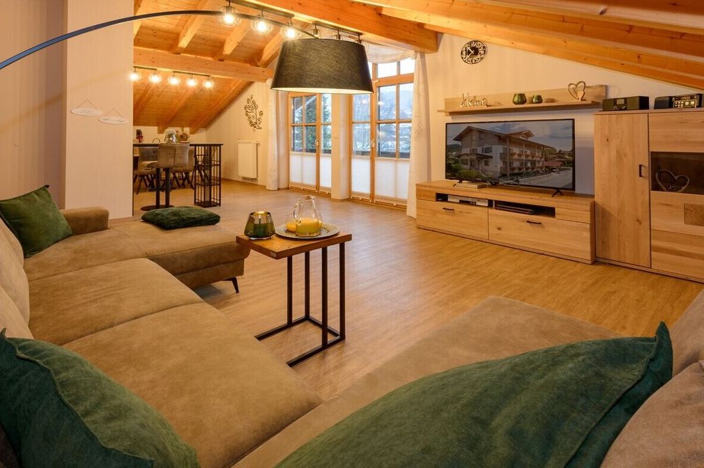 Un salon confortable avec un canapé, une table basse et un téléviseur. Au fond, on aperçoit un coin repas avec des chaises et une table.