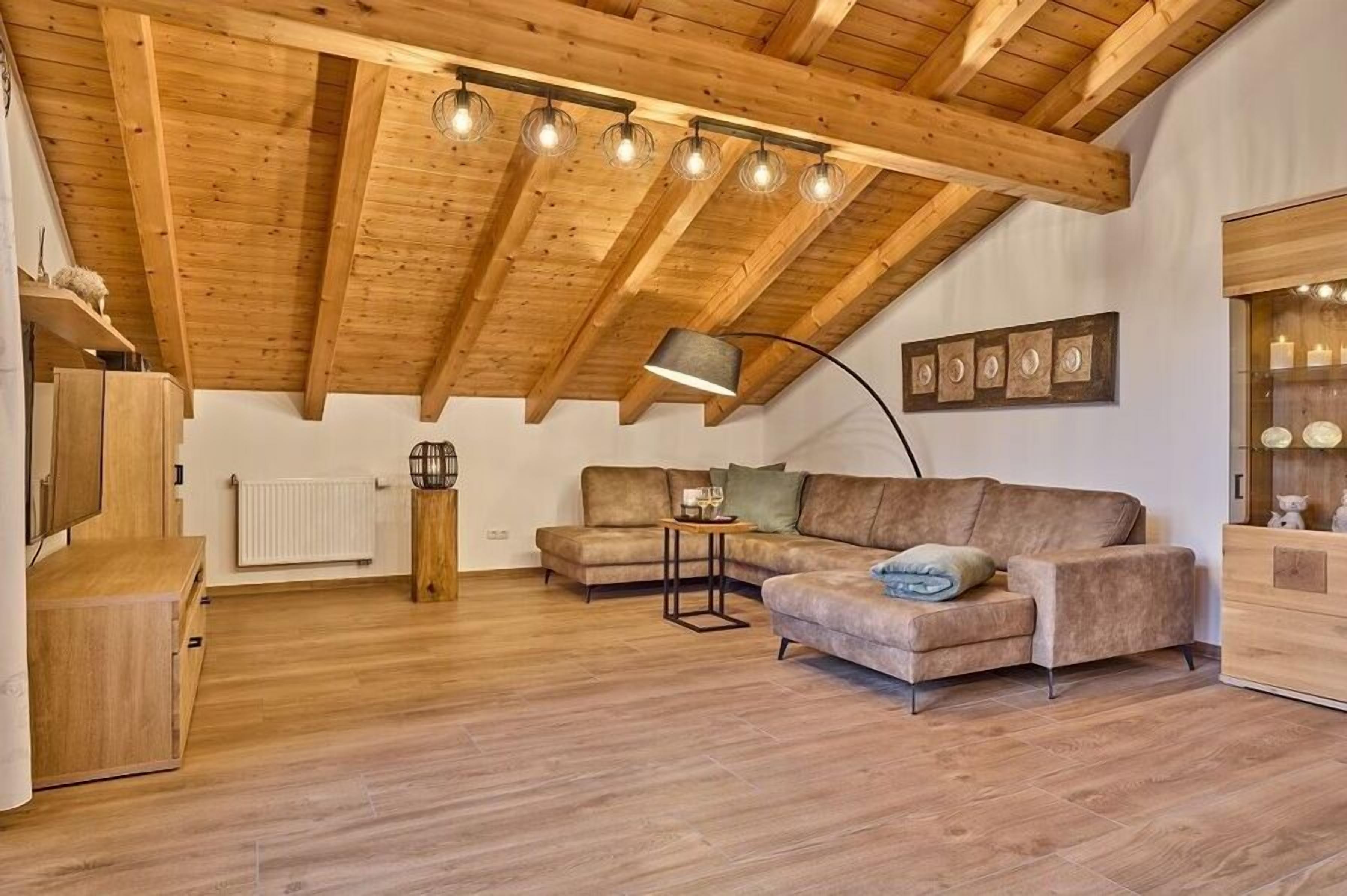 Ein geräumiges Loft mit freiliegenden Holzbalken, einem Ecksofa, einer Essecke und einer eingebauten Regaleinheit.
