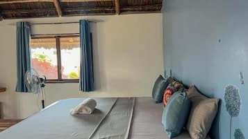 Een kamer met een bed, een raam met gordijnen, een ventilator en een wand met een vogeldecoratie.