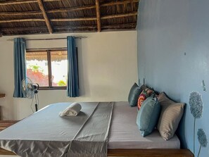 Une pièce avec un lit, une fenêtre avec des rideaux, un ventilateur et un mur décoré avec un motif d’oiseau.