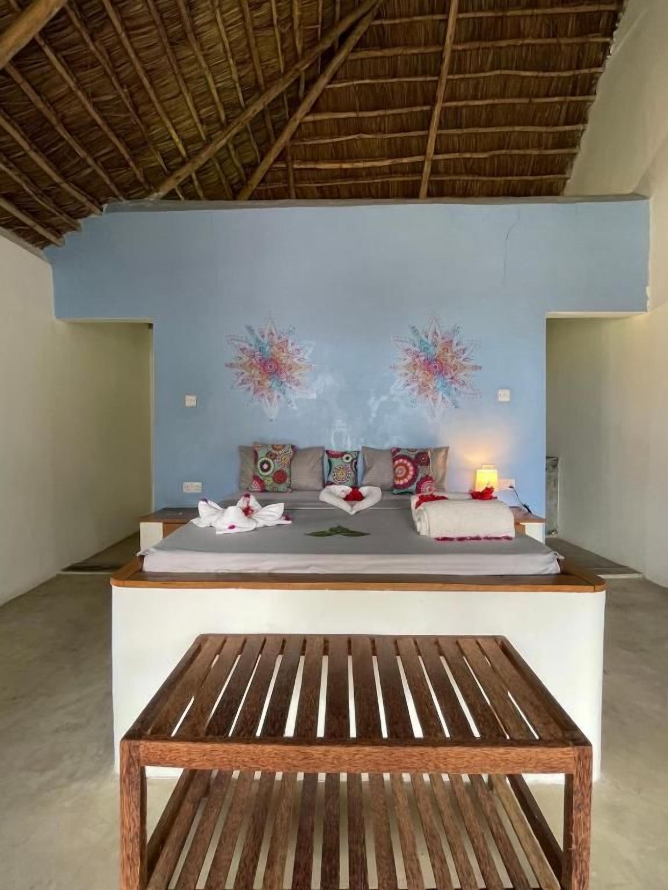 Een kamer met een bed, kussens, een nachtkastje en een wand met bloemwerk.