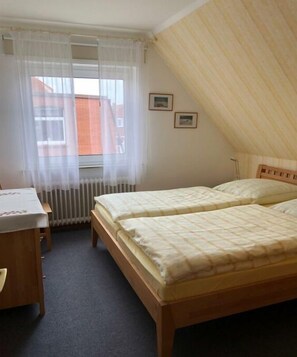 A bedroom with two beds, a wooden desk, a chair, a radiator, and a window with sheer curtains. - Holiday apartment in Juist with swimming pool (Juist)