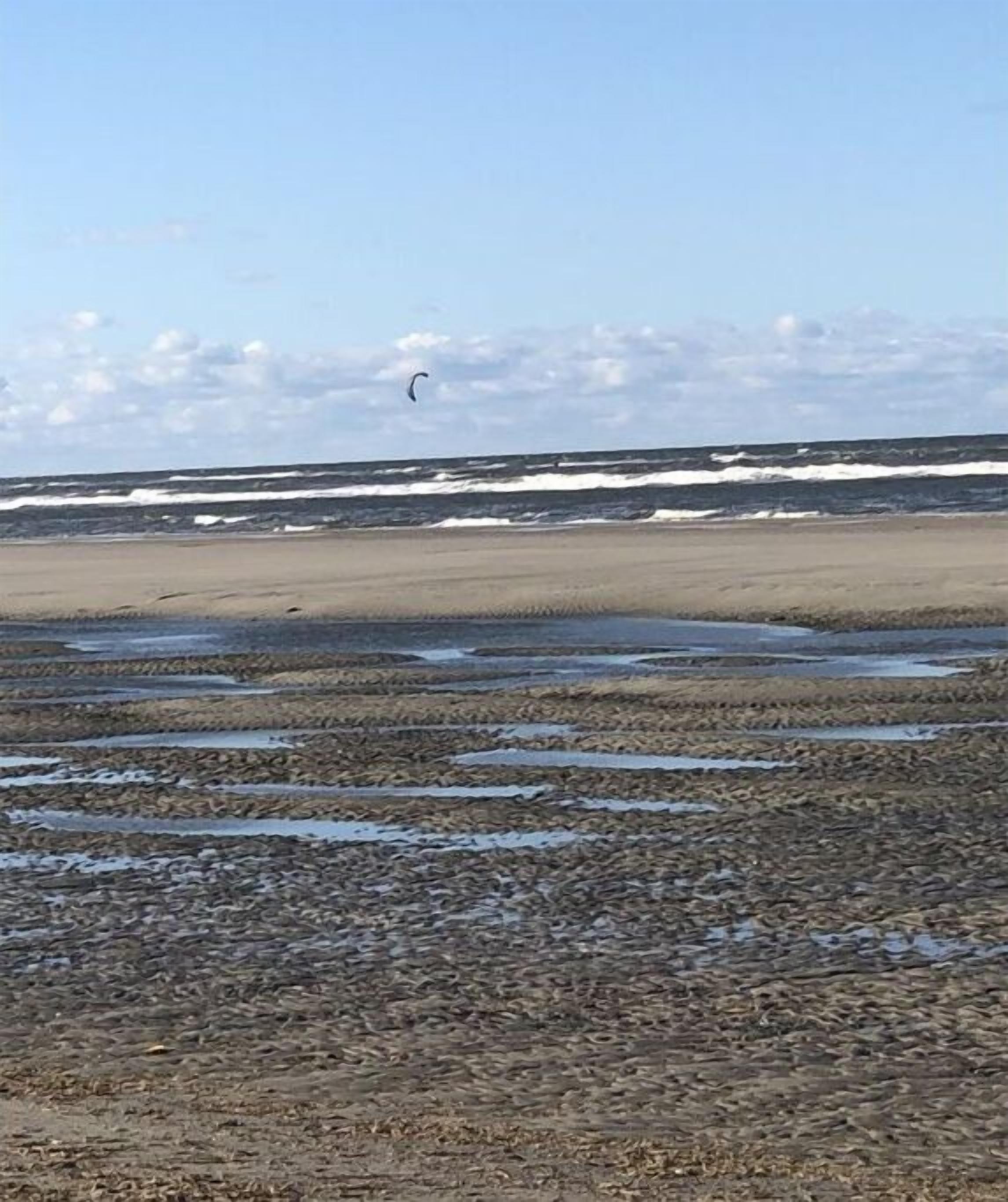 Ein Strand mit einer Person, die im Hintergrund Kitesurfen betreibt.