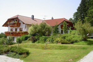 A two-story house with a red-tiled roof, a balcony with plants, and a grassy yard. - Holiday apartment with 1 bedroom (Passau - Salzweg)
