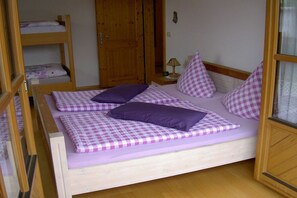 A single bed with a checkered bedspread and pillows, a wooden wardrobe, and a door in the background. - Holiday apartment with 1 bedroom (Passau - Salzweg)