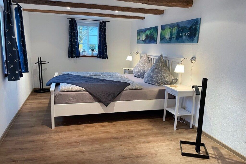 A bedroom with a bed, bedside tables, a window with curtains, and artwork on the wall.
