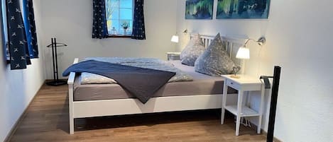 A bedroom with a bed, bedside tables, a window with curtains, and artwork on the wall.