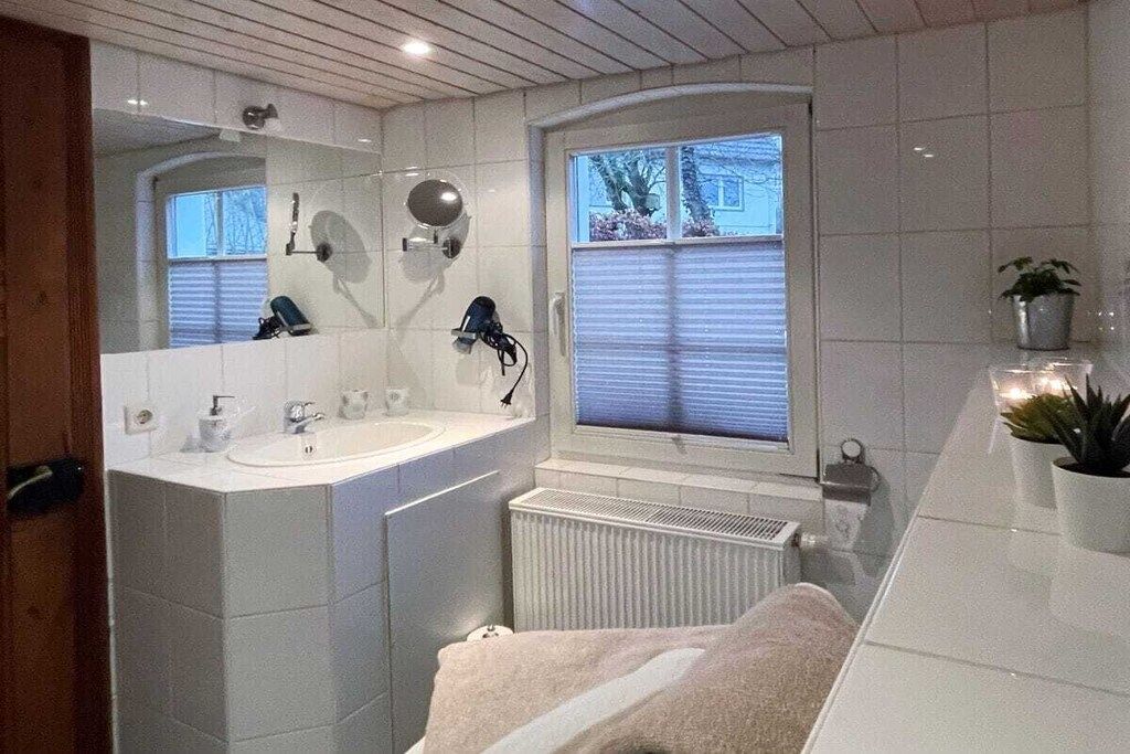 Une salle de bain moderne avec un grand miroir, un lavabo, une fenêtre avec des stores et une serviette sur le sol.