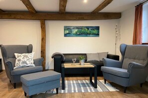 A living room with a black sofa, two grey armchairs, a small coffee table, and a painting on the wall. - Timber-framed holiday home 1764 (Eslohe)