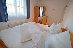Una camera d'albergo con un letto, un armadio in legno, una finestra con tende e un termosifone.
