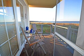 Un balcone con vista sulla spiaggia, un tavolo con sedie e un contenitore blu.