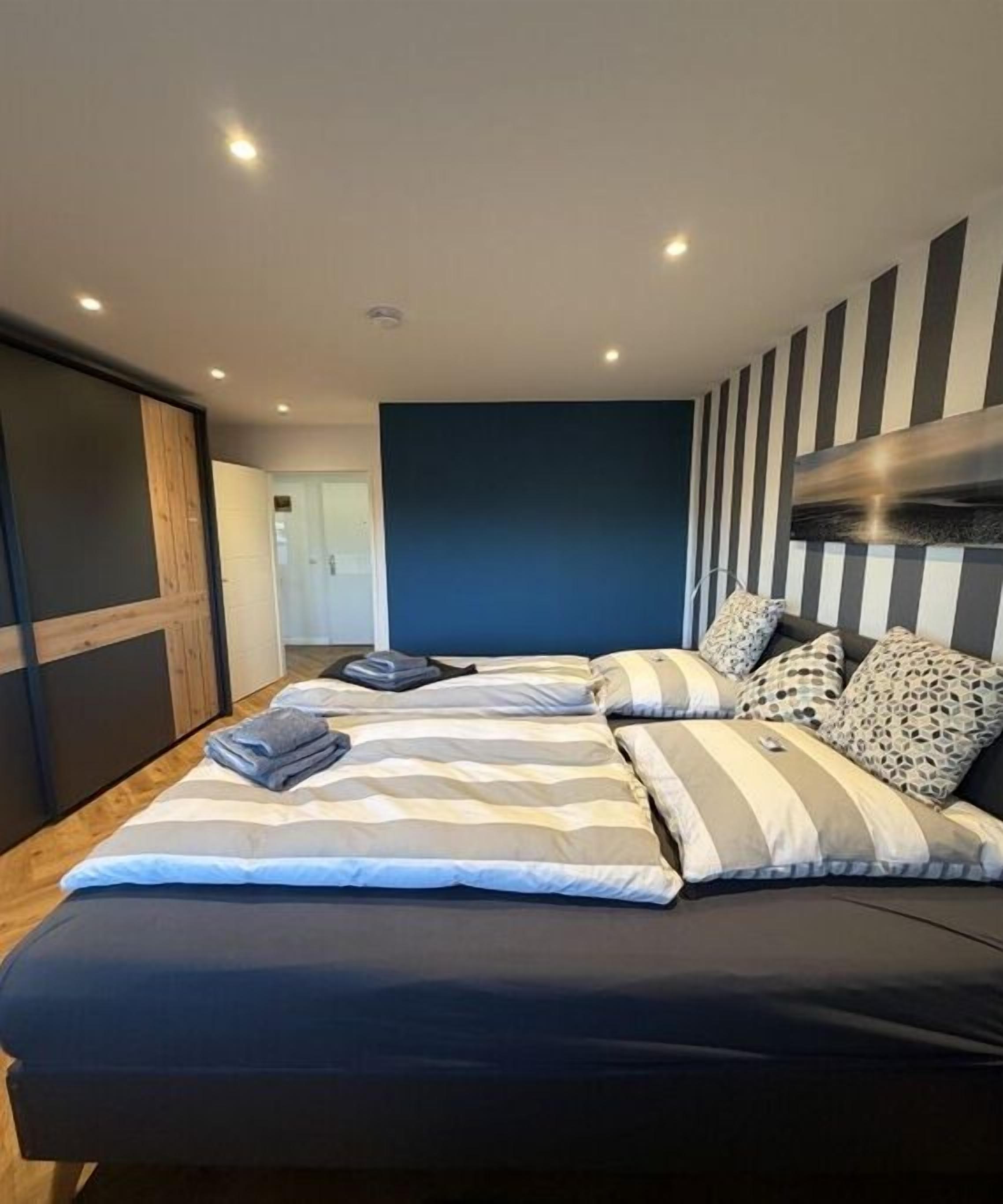 Un dormitorio moderno con una cama grande, cabecera a rayas y vista a un pasillo.