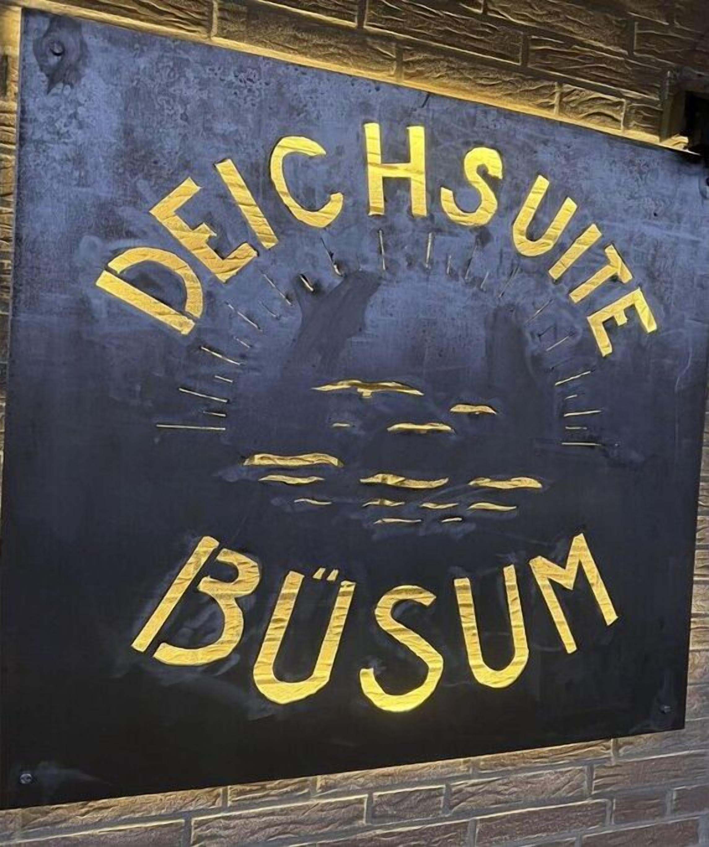 A sign with the words 'DEICHSUITE BUSUM' in gold lettering on a dark background.