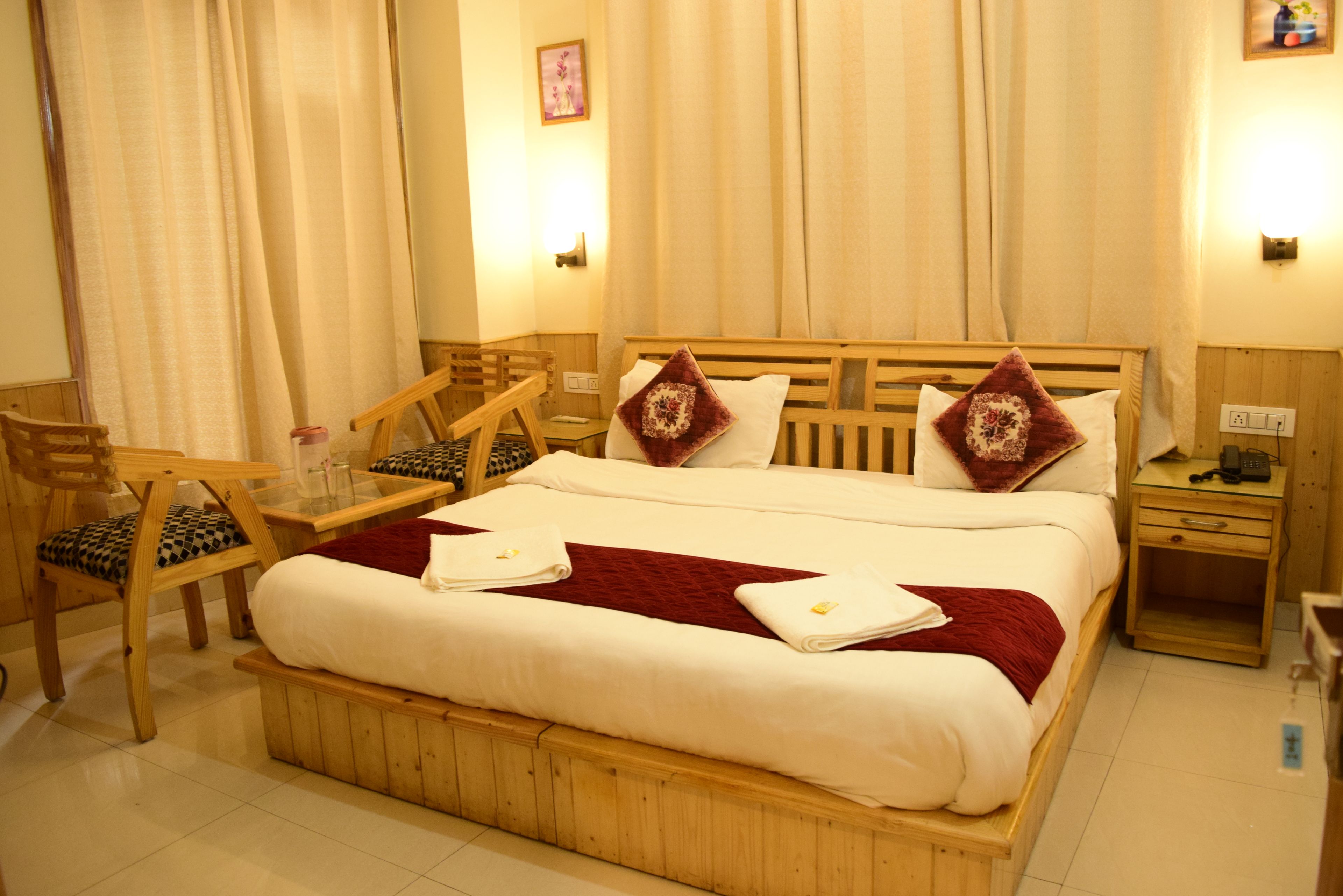 A hotel room with a wooden bed, two nightstands, a chair, a small table, and a mirror.