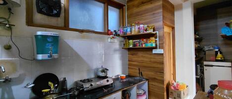 A kitchen with a water dispenser, stove, and shelves with various food items.