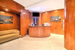 A reception area with a wooden reception desk, a sofa, and wall-mounted decor. - Palette Sanur near Beach (Denpasar)