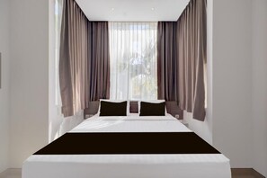 A modern bedroom with a large bed, sheer curtains, and a view of greenery outside. - Palette Sanur near Beach (Denpasar)