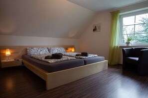 Ein modernes Schlafzimmer mit einem Bett, Nachttischlampen, einem Fenster mit Vorhängen und einem Sessel.
