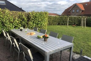 Ein Essbereich im Freien mit einem Tisch für vier Personen, umgeben von Stühlen, in einem Garten mit einer Hecke und einer Schaukel.