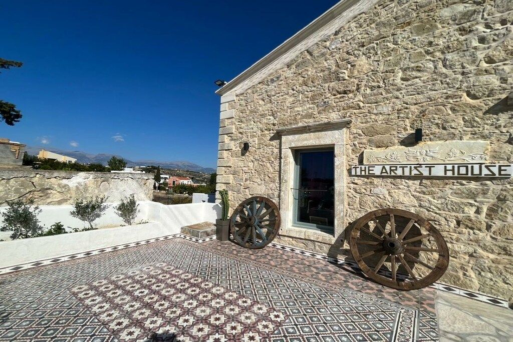 A stone building with a sign reading 'The Artist House' and two large wooden wheels.